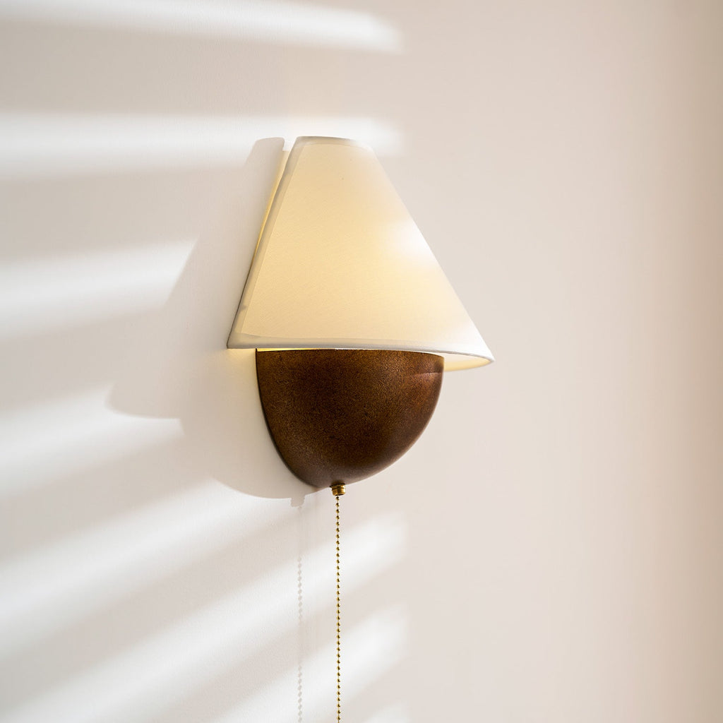 Close side view of this lit Clérachic wall light, showing the soft glow in the shade against a blush wall.