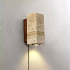 Square-sided Clérachic wall light in banded travertine, with a walnut-colour plate behind and its downlight lit on a grey wall.