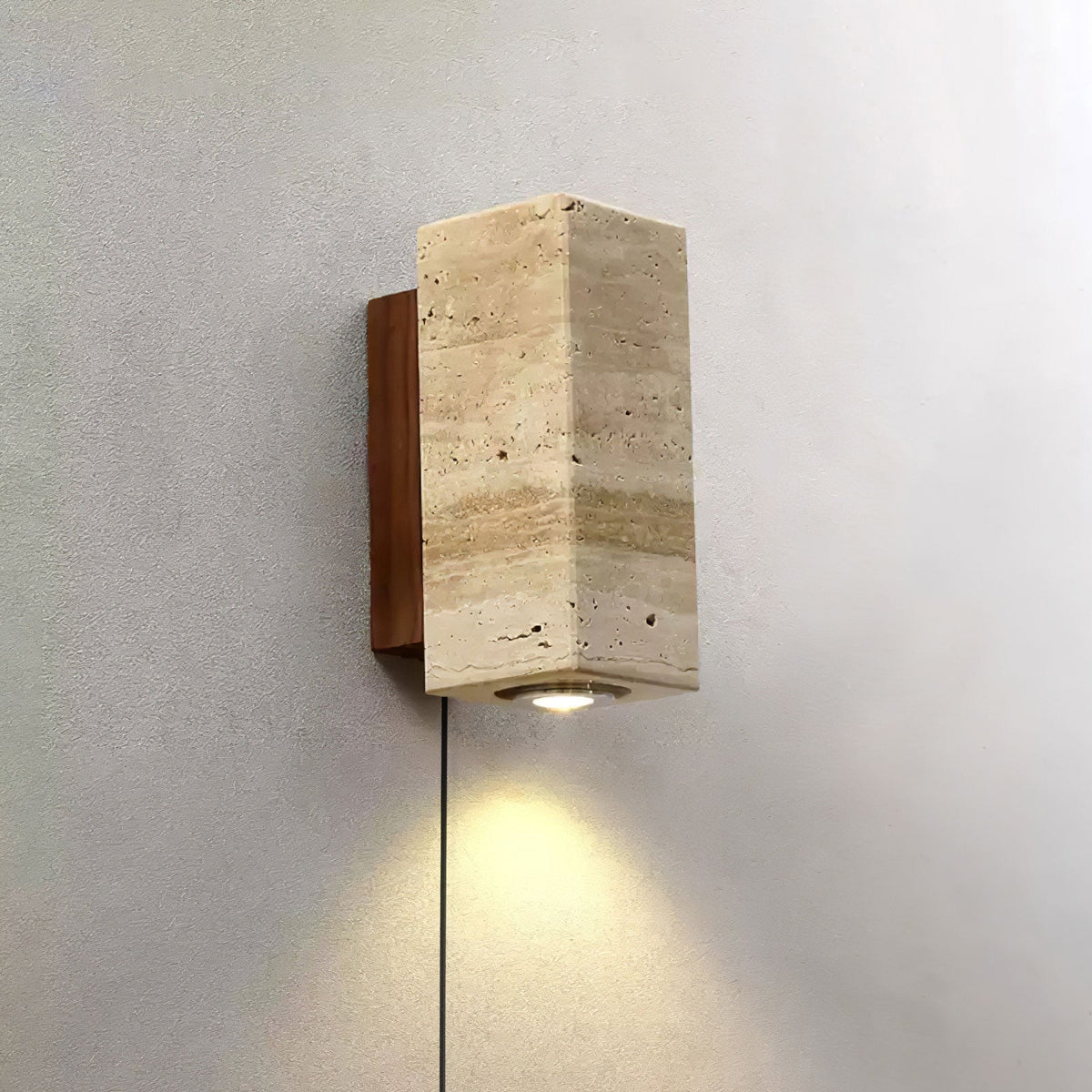 Square-sided Clérachic wall light in banded travertine, with a walnut-colour plate behind and its downlight lit on a grey wall.