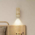 Slim rectangular travertine wall light from Clérachic above a woven rattan headboard, with a cone of light below it.