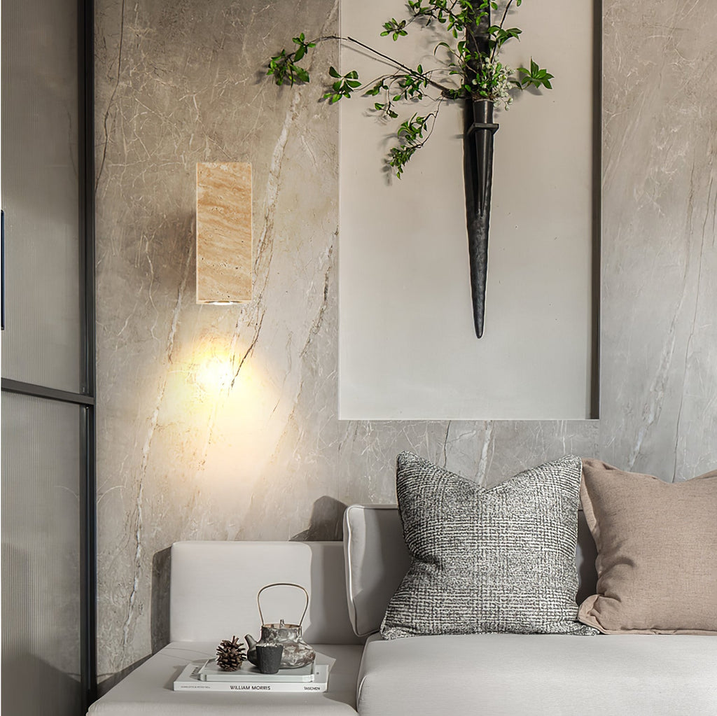 Small Clérachic travertine wall light on a marbled wall above a grey sofa, with a tea set and a branch in a tall vase.