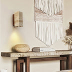 Clérachic travertine wall light above a stone console with a large rounded stone, books and a white woven wall hanging.