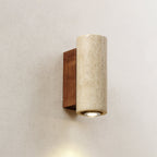 Close view of a cylindrical Clérachic wall light, its travertine shade pitted with natural holes and a lit round downlight.