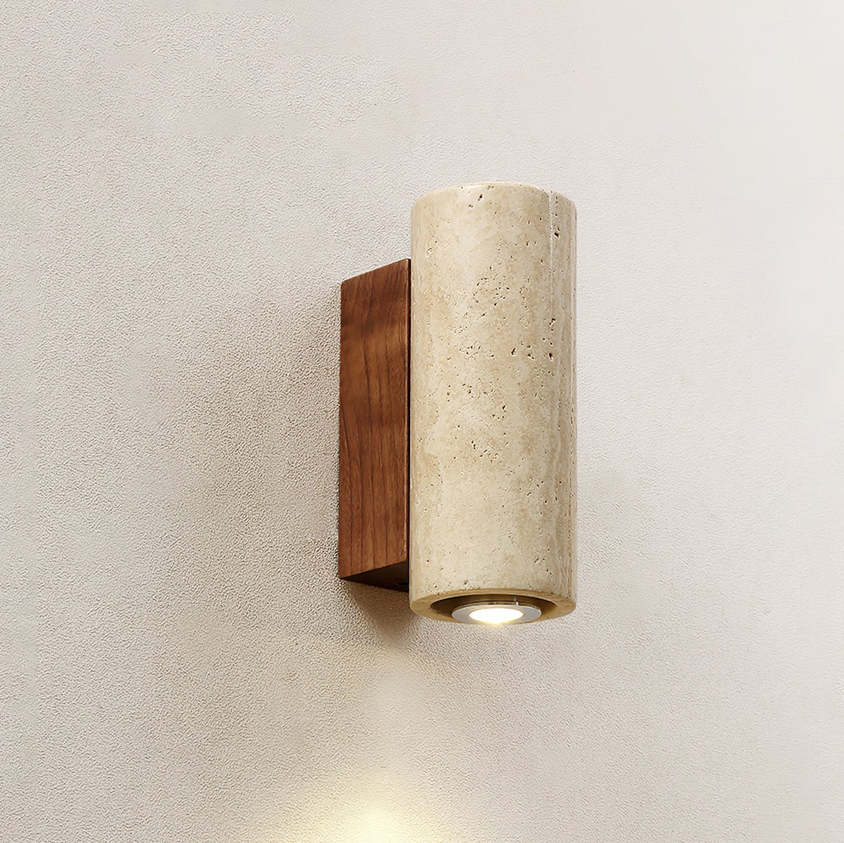 Close view of a cylindrical Clérachic wall light, its travertine shade pitted with natural holes and a lit round downlight.