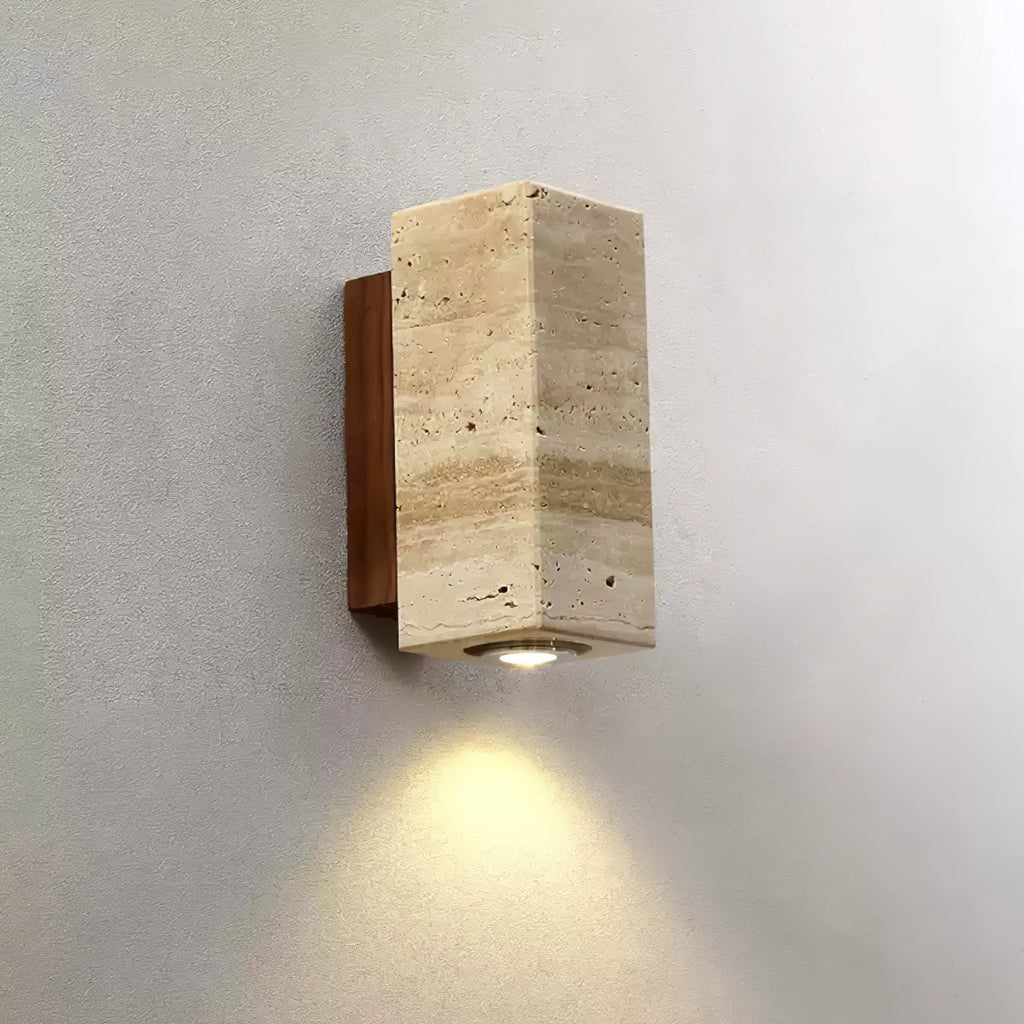 Close view of the veined, banded travertine on this square-sided Clérachic wall light, with warm light on the wall below.