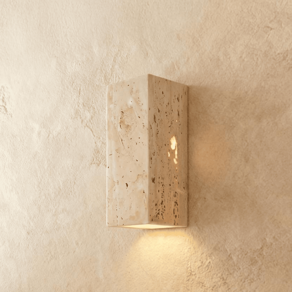 Clérachic rectangular travertine wall light with a pitted, veined stone surface, glowing warm from its base onto the wall.