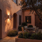 Clérachic tall travertine wall light glowing warm at dusk on a terracotta courtyard wall above lavender and a bistro table.