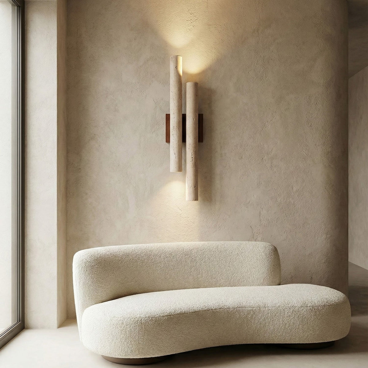 This Clérachic travertine wall light throws light up and down a plaster wall, above a curved boucle sofa by a window.