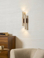 A lit Clérachic travertine wall light seen from a slight angle, with a stack of books on the chest below.