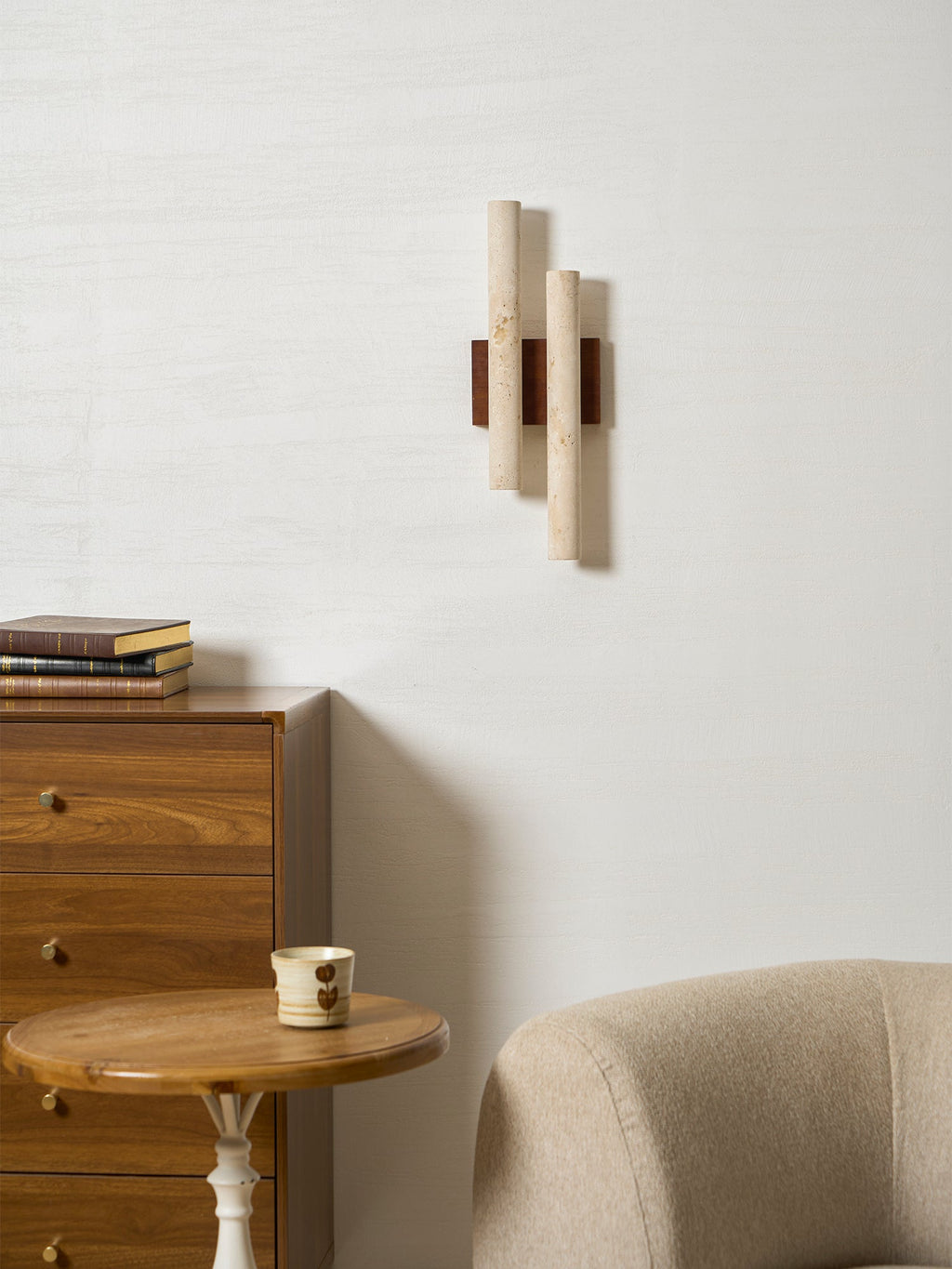 An unlit Clérachic wall light above a wooden chest and a round side table, with a beige chair at the corner of the frame.
