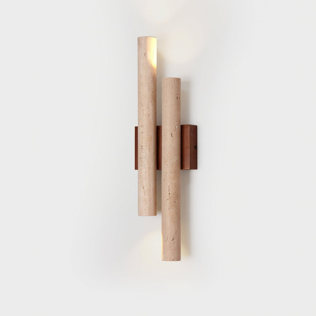 A Clérachic wall light with a travertine tube open at the top, lit on a pale backdrop, with its walnut plate behind.