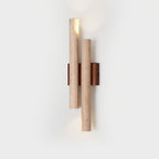 A Clérachic wall light with a travertine tube open at the top, lit on a pale backdrop, with its walnut plate behind.
