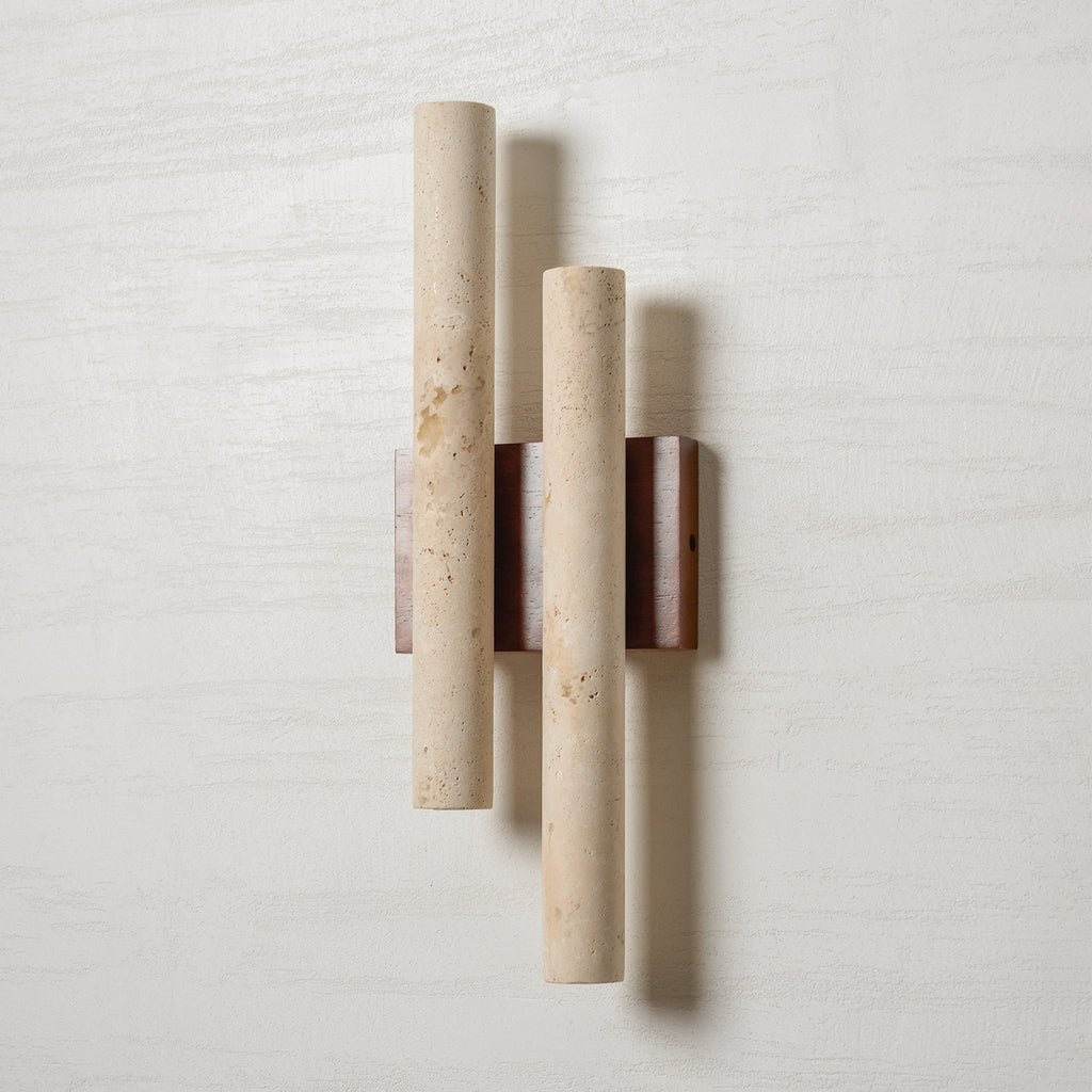 A Clérachic wall light on a white wall, its two travertine tubes showing natural pits and a walnut-wood backplate.