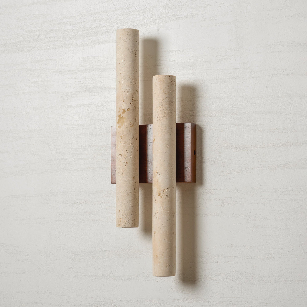 A Clérachic wall light on a white wall, its two travertine tubes showing natural pits and a walnut-wood backplate.