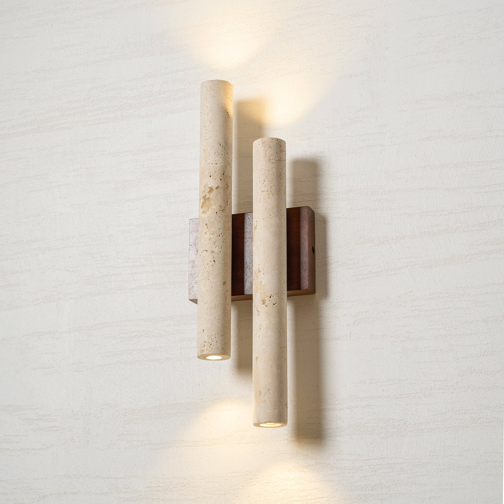 Looking up at the lit Clérachic wall light, with a small round opening at the base of each travertine tube.