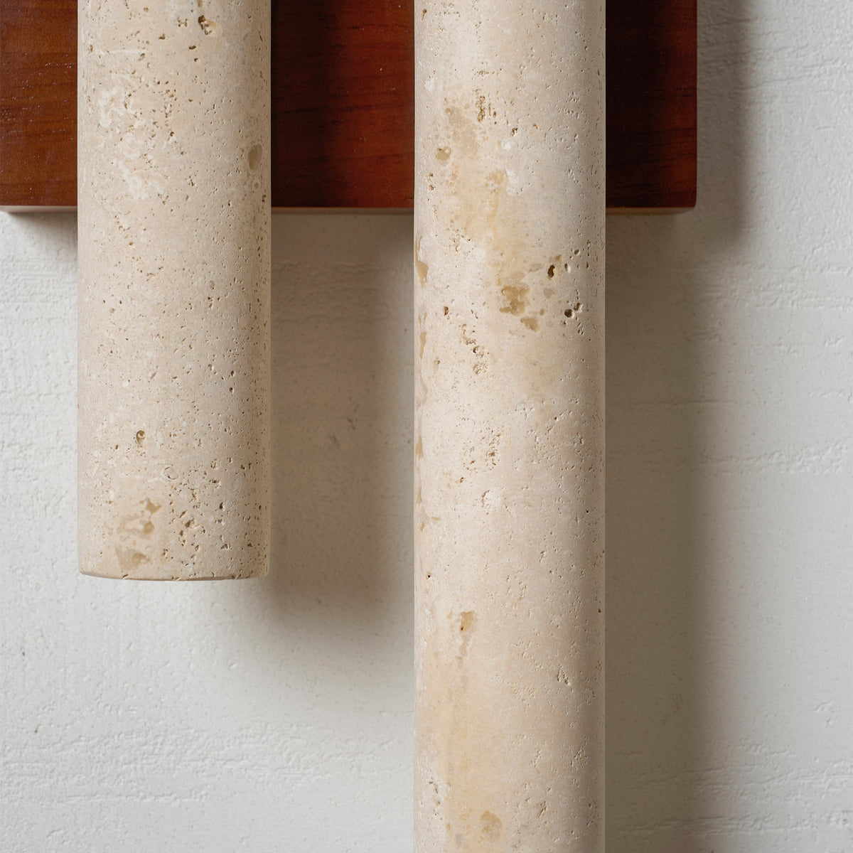 Close view of the pitted, honey-coloured travertine tubes and the walnut-wood backplate of this Clérachic wall light.