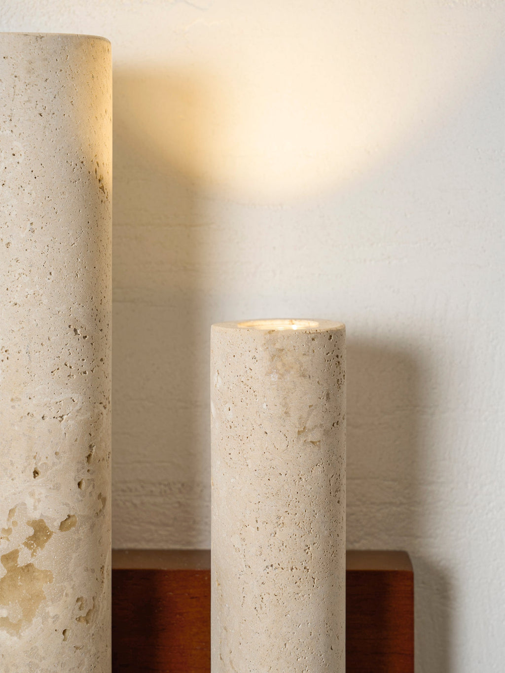 Detail of the open tops of two travertine tubes on this Clérachic wall light, with warm light coming from the shorter one.
