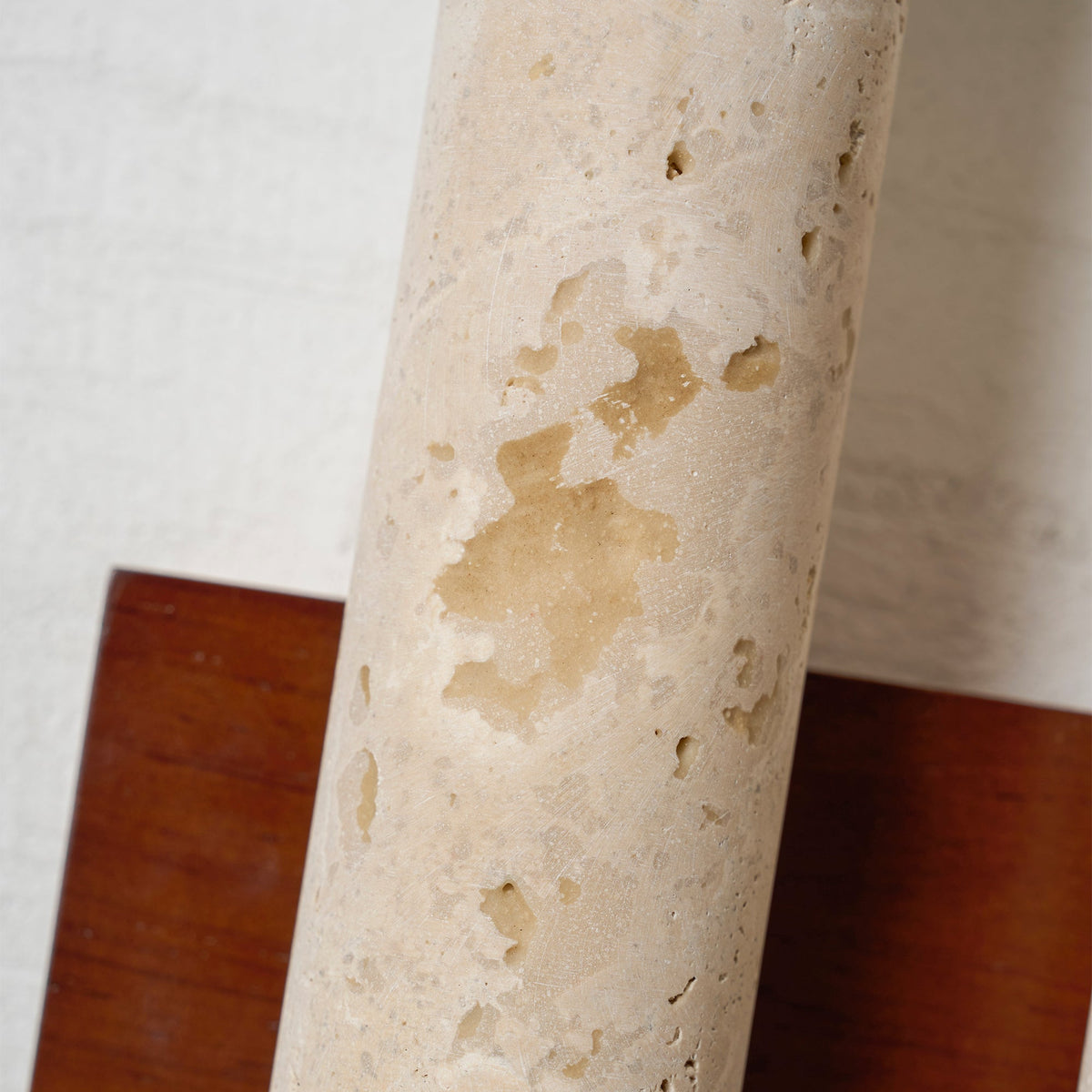 Close view of the natural pits and honey-toned patches in the travertine tube of this Clérachic wall light, against walnut wood.