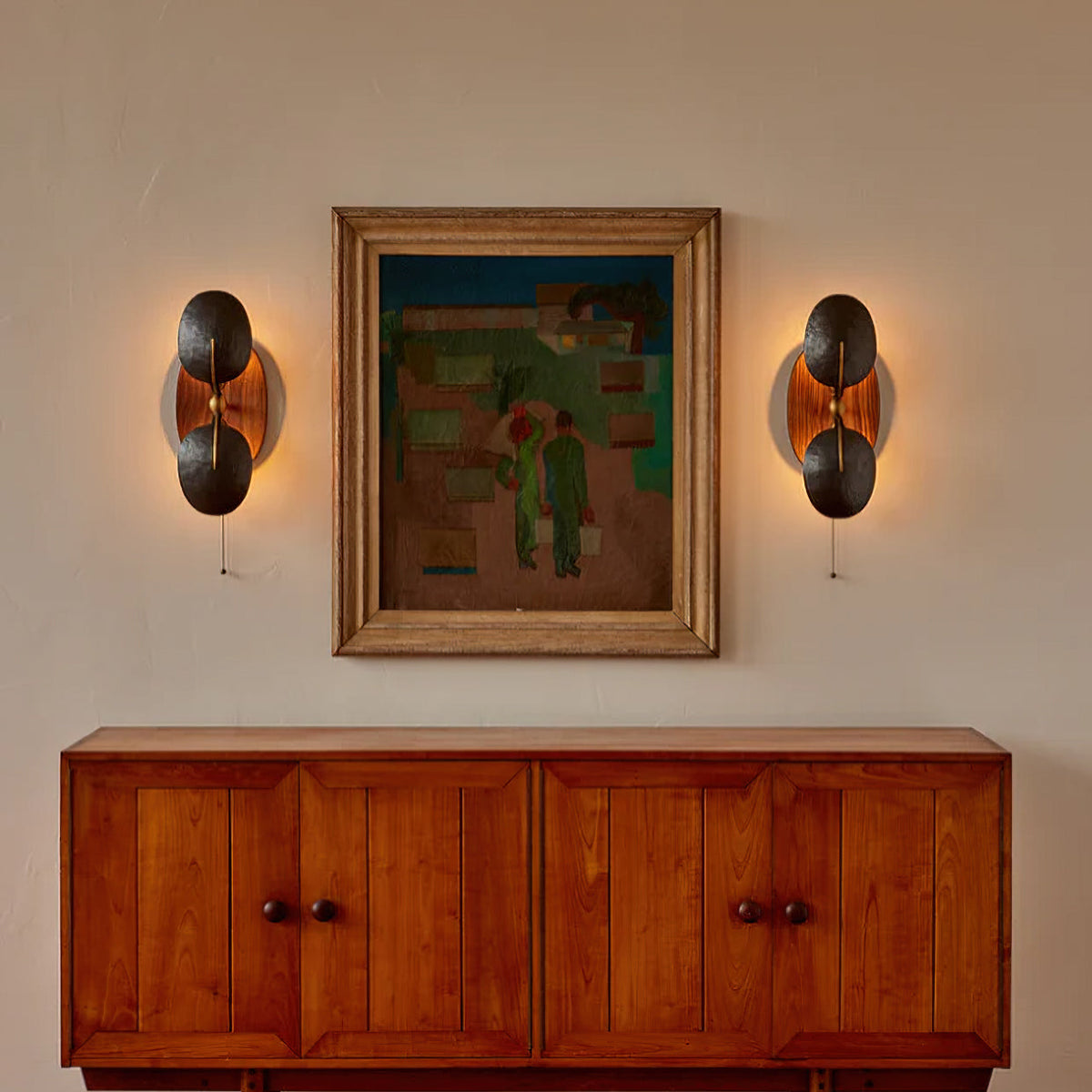 A pair of Clérachic wall lights glowing either side of a framed painting, above a teak-toned sideboard with panelled doors.