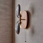 Side view of this Clérachic wall light, with two filament bulbs showing beside the dark shades and a brass-toned pull chain hanging below.