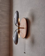 Angled view of this Clérachic wall light, its two shades curving on slim arms over a walnut backplate, with the bulbs visible.