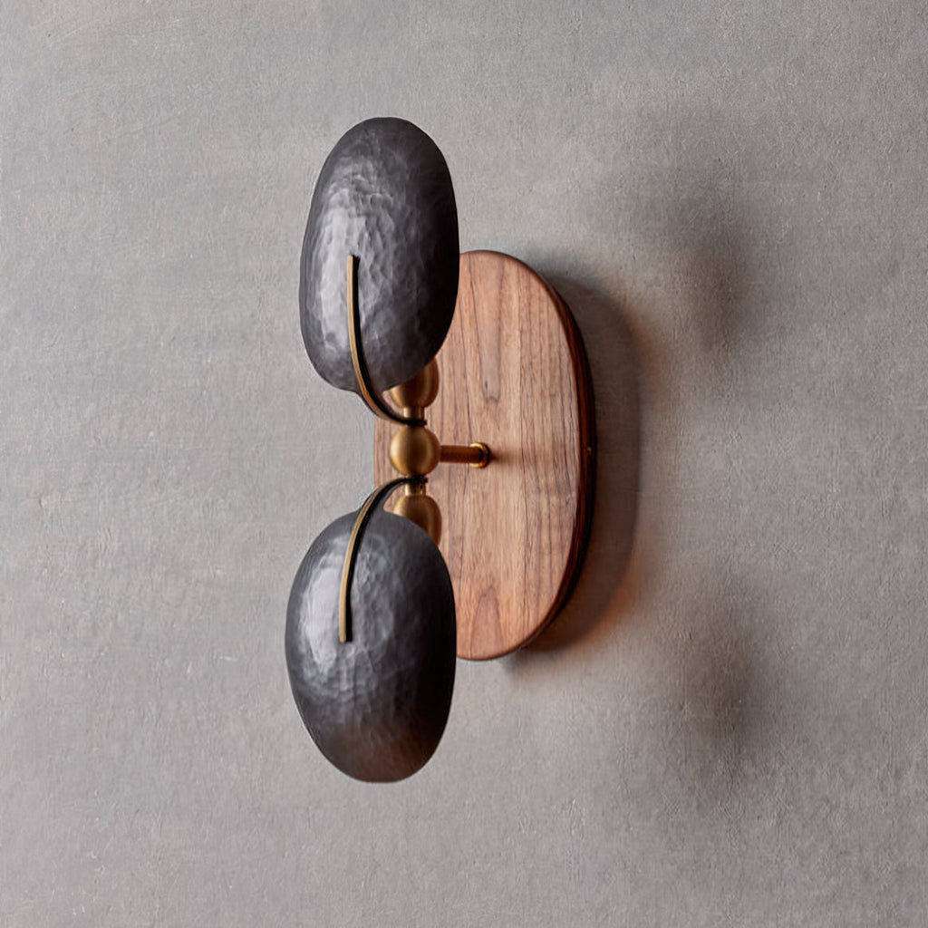 This Clérachic wall light unlit on a grey wall, showing two hammered dark shades, brass joints and an oval walnut backplate.