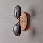 This Clérachic wall light unlit on a grey wall, showing two hammered dark shades, brass joints and an oval walnut backplate.
