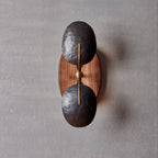Front view of this Clérachic wall light, with a brass rod and ball joint between two dark shades on an oval walnut backplate.