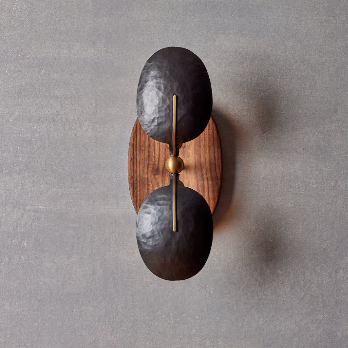 Front view of this Clérachic wall light, with a brass rod and ball joint between two dark shades on an oval walnut backplate.