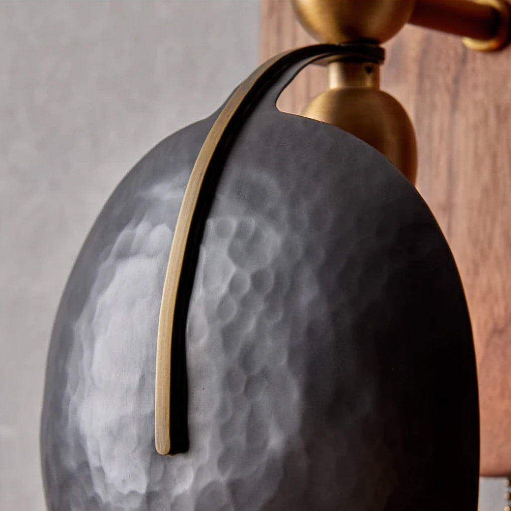 Close view of the hammered finish on one dark shade of this Clérachic wall light, with a slim brass strip down its face.