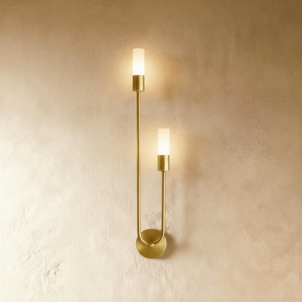 Clérachic brass wall light with two slim frosted cylinder diffusers on a U-shaped arm and round wall plate, lit warm on plaster.