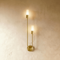 Clérachic brass wall light with two slim frosted cylinder diffusers on a U-shaped arm and round wall plate, lit warm on plaster.