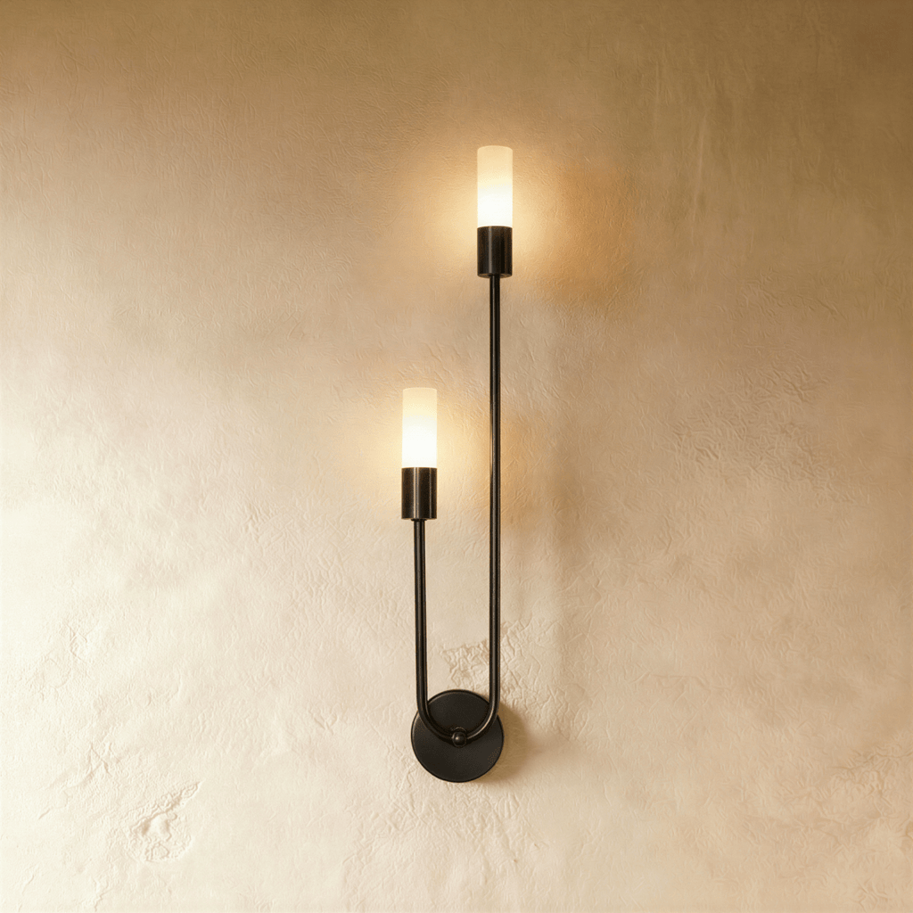 Clérachic black wall light with two glowing frosted cylinder diffusers on a slim U-shaped arm and round plate, on plaster.