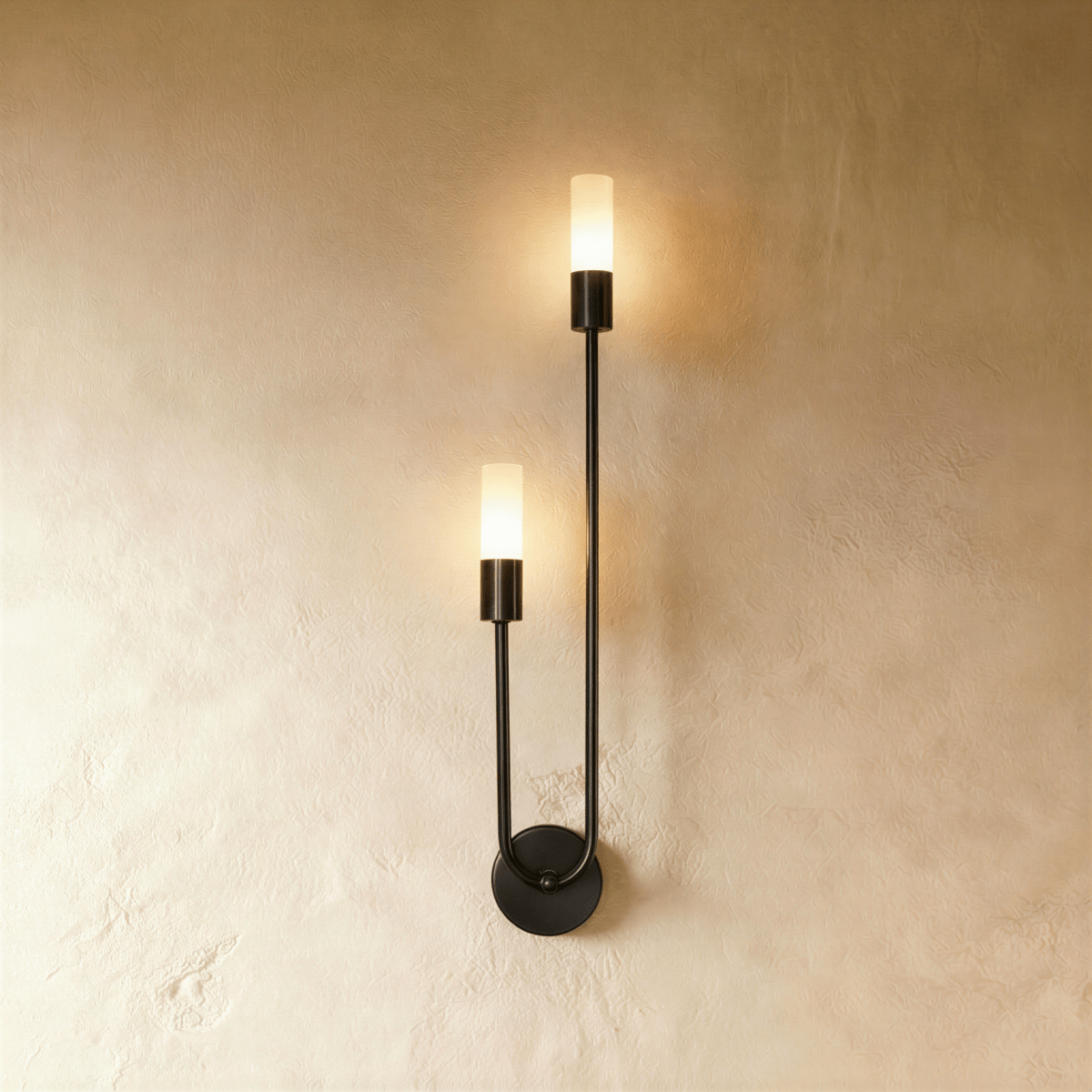Clérachic black wall light with two glowing frosted cylinder diffusers on a slim U-shaped arm and round plate, on plaster.