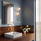 Clérachic brass wall light beside a brass-framed mirror above a tiled washbasin, against a blue plaster bathroom wall.
