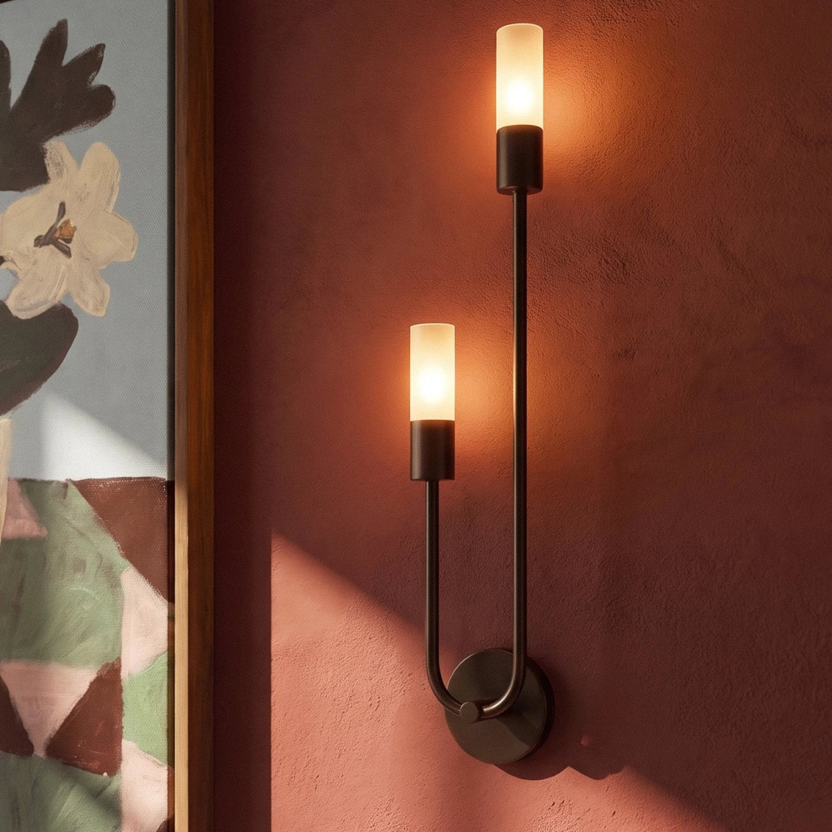 Clérachic black wall light close-up, two glowing frosted cylinder diffusers on a slim U-shaped arm against a terracotta wall.