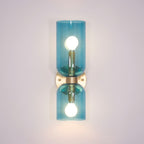 Blue glass cylinders catch the light on this gold Clérachic sconce against a lilac wall.