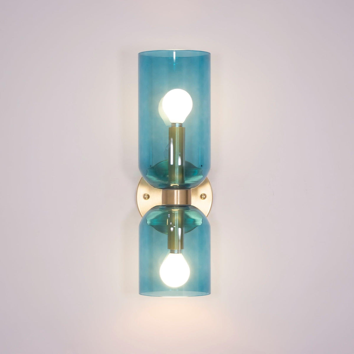 Blue glass cylinders catch the light on this gold Clérachic sconce against a lilac wall.