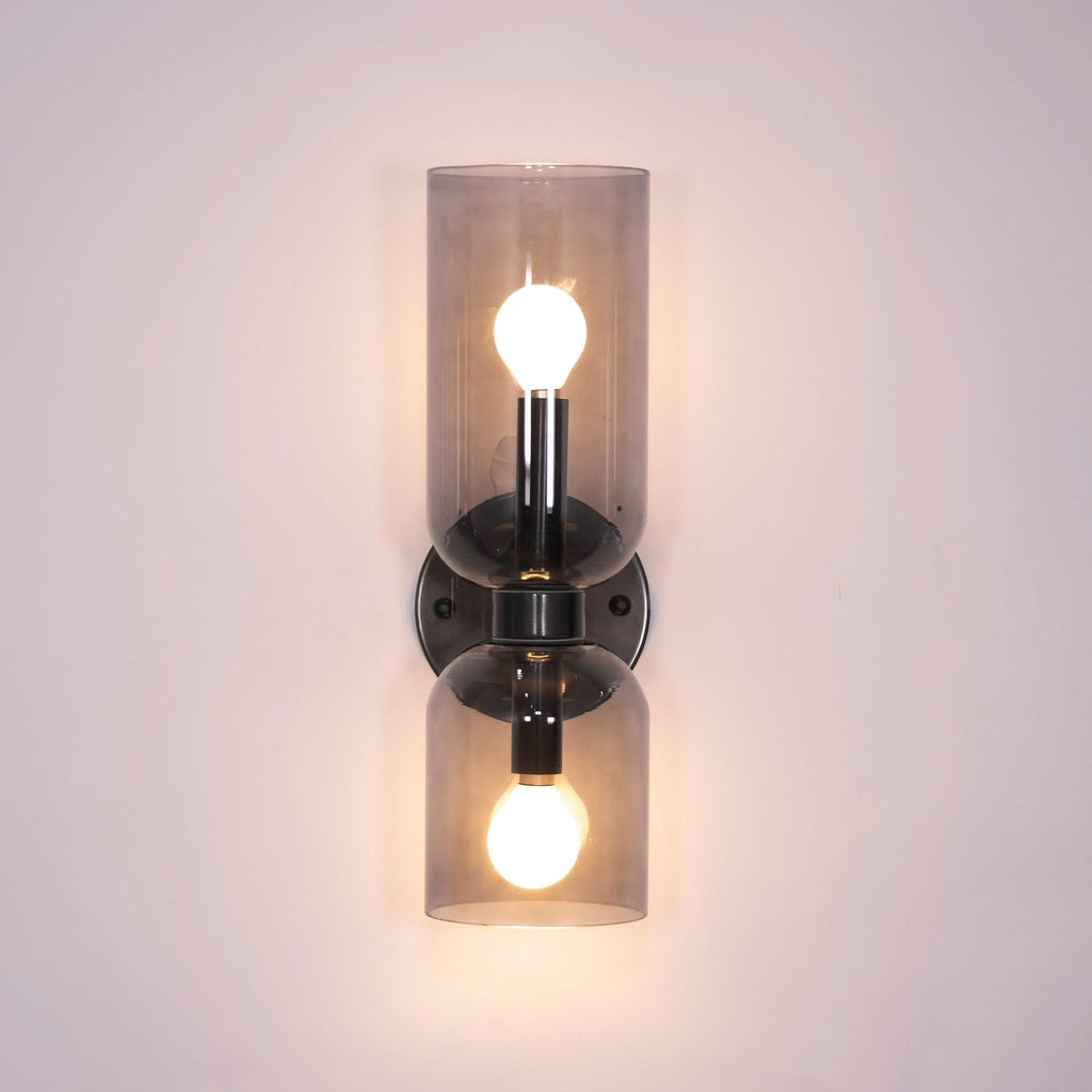 Smoke grey glass cylinders let the bulbs show through on this matt black Clérachic sconce.