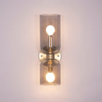 In gold, this Clérachic wall light holds smoke grey glass cylinders with the bulbs visible.