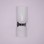 Unlit against a pale lilac backdrop, this gunmetal Clérachic wall light shows its opal glass shades.