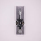 A gunmetal Clérachic sconce holds smoke grey glass cylinders, unlit against a lilac backdrop.