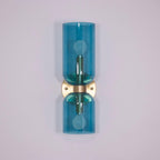 In gold, this Clérachic sconce's blue glass cylinders stand against a pale lilac wall.