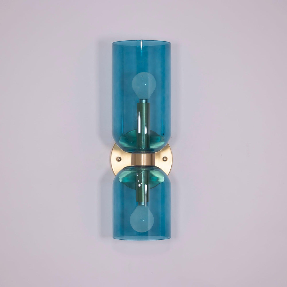 In gold, this Clérachic sconce's blue glass cylinders stand against a pale lilac wall.