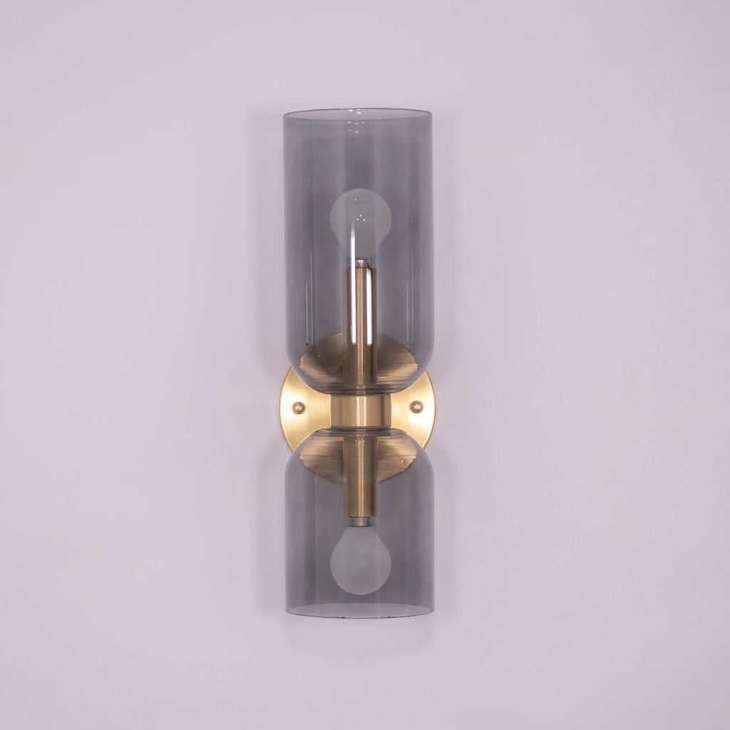 Smoke grey glass cylinders sit on this gold Clérachic wall light against a lilac backdrop.
