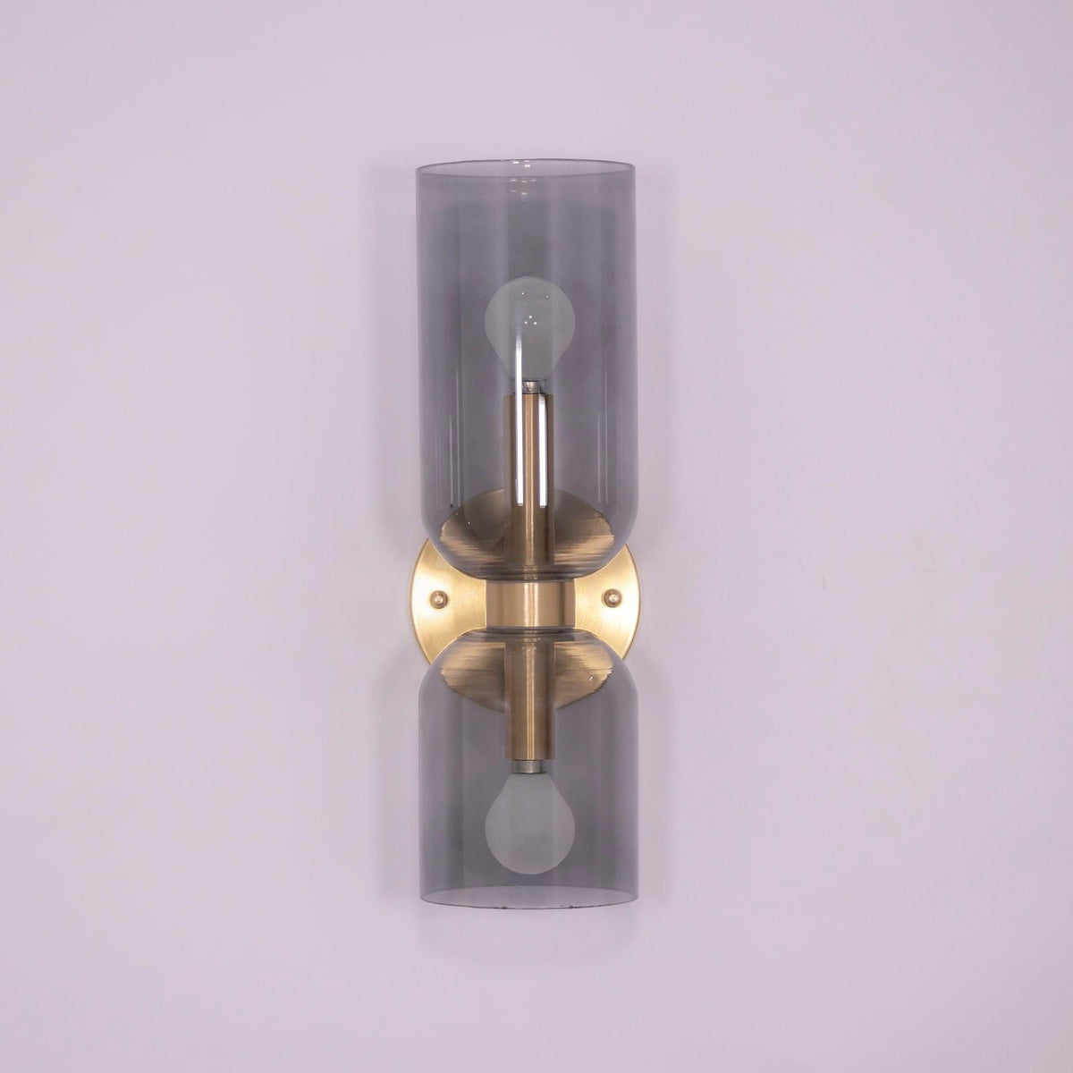 Smoke grey glass cylinders sit on this gold Clérachic wall light against a lilac backdrop.