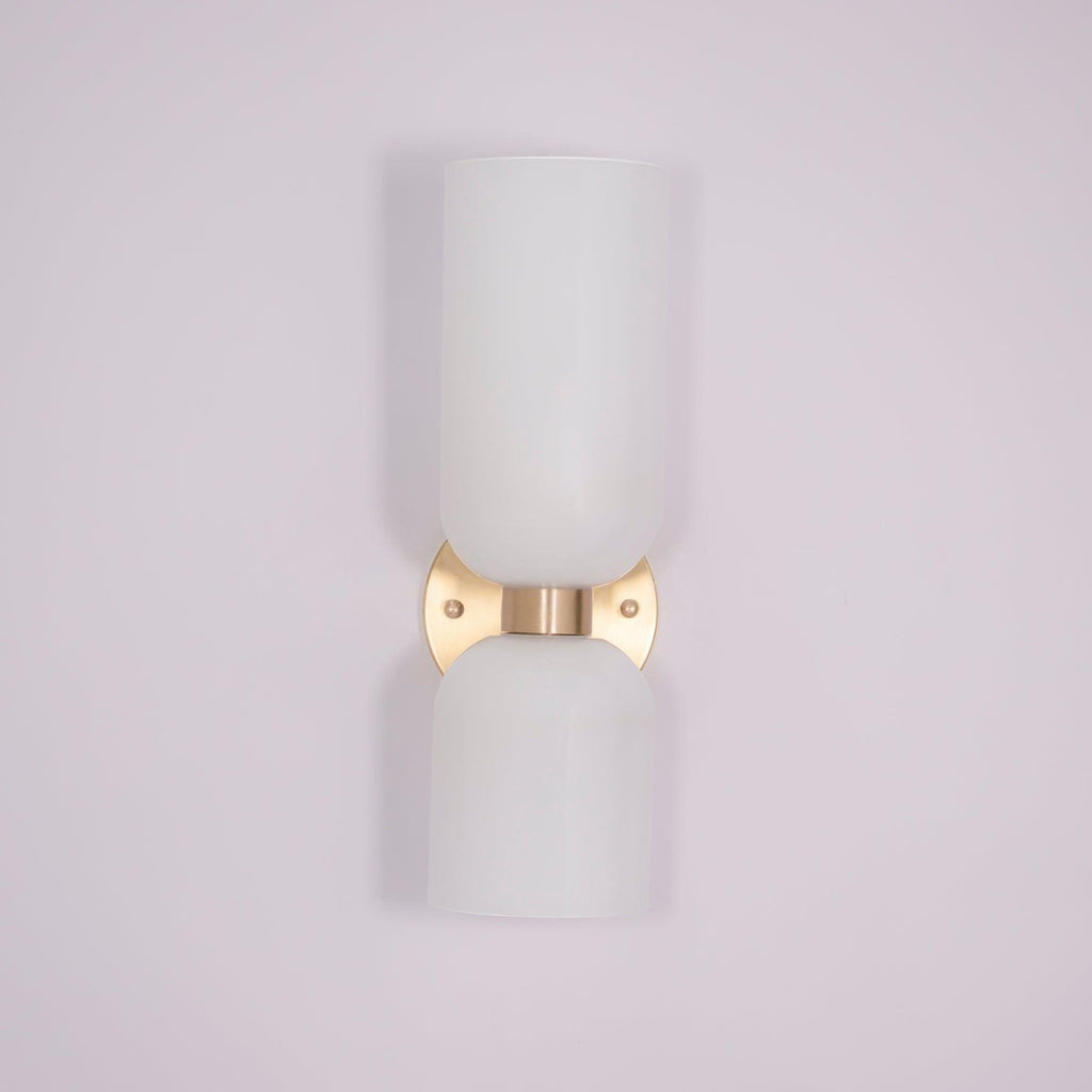 A tapered white glass shade tops this gold Clérachic sconce against a soft lilac backdrop.