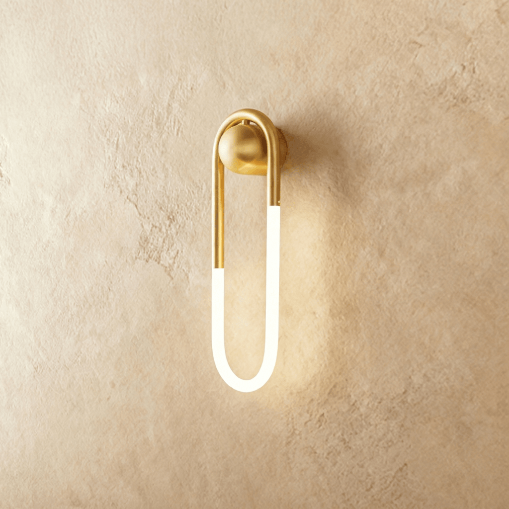 Clérachic elongated U-shaped wall light in brushed brass with a frosted glowing tube, mounted on warm limewash plaster.