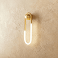 Clérachic elongated U-shaped wall light in brushed brass with a frosted glowing tube, mounted on warm limewash plaster.