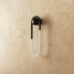 Clérachic U-shaped wall light in matt black with its frosted tube switched off, seen against warm limewash plaster.